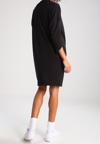 Robe noire oversize à manches courtes avec une silhouette ample et un ourlet arrondi, portée avec des chaussettes courtes blanches et des baskets.