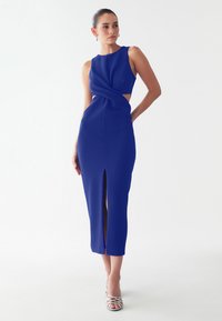 Form-fitting, sleeveless blue dress with twisted bodice detail and side cutouts. Features a thigh-high slit and smooth texture.