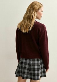 Pull en laine bordeaux au design court associé à une jupe à carreaux noir et blanc avec un ourlet évasé.