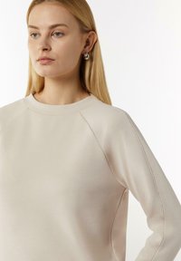 Lichtbeige sweatshirt met een ronde hals, raglan mouwen, platte naden en een soepele textuur. Geen zichtbare patronen of hardware.