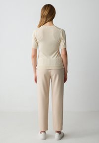 Top a maniche corte di colore crema in maglia, con dettagli a costine, abbinato a pantaloni leggeri beige. Design semplice, vestibilità rilassata e texture morbida.
