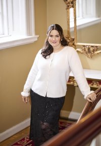White, fluffy cardigan with button closure and pearl accents, paired with a black, sequined skirt featuring a geometric pattern.