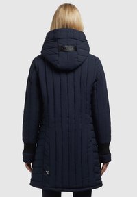 Navy padded long coat with vertical quilting, a large hood, and ribbed cuffs. Features a logo tag on the back and a rounded hem.