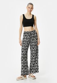 Mustan lyhyen topin kaverina on leveälahkeiset housut, joissa on monochrome-timanttikuvio. Mallilla on päällään vaaleat korokepohjat.