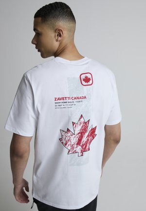 Ung mann sett bakfra iført en hvit T-skjorte med røde lønneblad-grafikker og teksten "Zavetti Canada" med stedkoordinater.