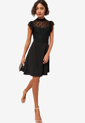 Černé šaty s krajkovým korzetem a volánkovými rukávy, se splývavou sukní. Doplněné malou kabelkou a sandály na podpatku.