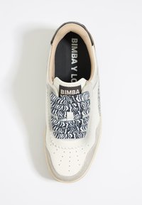 Zapatilla blanca con acentos de ante gris, cordones elásticos con patrón de cebra, puntera perforada y logo "BIMBA Y LOLA" en la lengua.