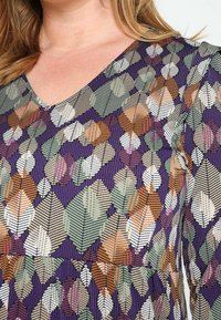 Robe à manches longues avec un fond violet et un motif de feuilles multicolores en vert, marron et blanc. Col en V avec tissu texturé.