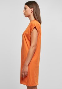 Rövid, narancssárga, pamut t-shirt ruha felgöngyölt ujjakkal. Egyenes szabású, térdfelett érő, minimális részletezéssel.