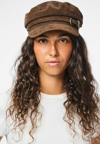 Gorra de ante marrón con una corona redondeada, dos bandas horizontales y un detalle de hebilla de metal. Tejido texturizado y diseño clásico.