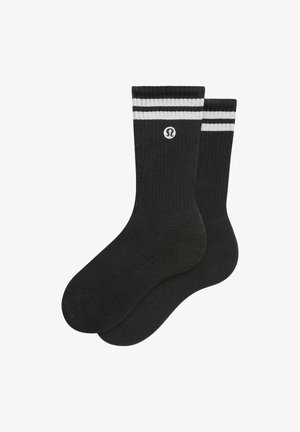 Chaussettes de sport noires avec des rayures blanches en haut et un logo. Texture tricotée avec un design côtelé. Longueur standard à la cheville.