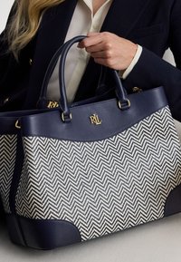 Granatowa skórzana torebka z tkaniną w wzór jodełki. Wyposażona w złote okucia i dwa okrągłe uchwyty. Uzupełniona ciemnym skórzanym wykończeniem.