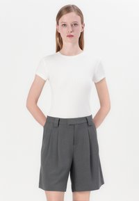 Hvit ribbet t-skjorte med korte ermer, kombinert med grå høyhårete plisserte shorts; slank design uten synlige mønstre eller detaljer.