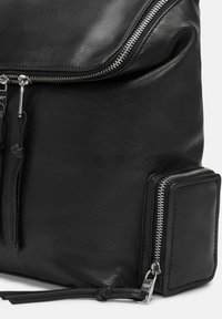 Sac à dos en cuir noir avec fermeture à glissière en haut, poche à glissière sur le côté, et texture lisse avec des détails subtils et des accents en métal.