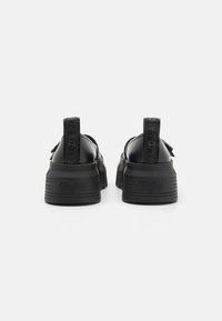 Svarta plattformssneakers med en slät läderöverdel, texturerad gummisula och tygdragflikar med logotypdetaljer på baksidan.