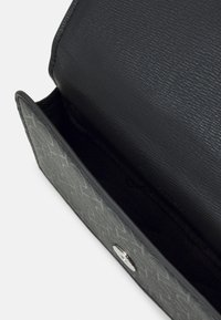 Szary i czarny portfel z teksturowanym klapkiem i srebrnym zatrzaskiem, pokazany otwarty, ujawniający pusty wnętrze z wzorzystą powierzchnią zewnętrzną.