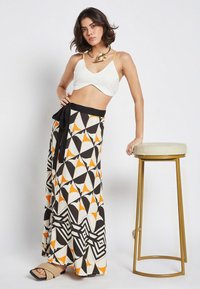 White cropped top with a deep V-neck; patterned maxi skirt in black, white, orange, and geometric shapes; black waistband; gold accessories.