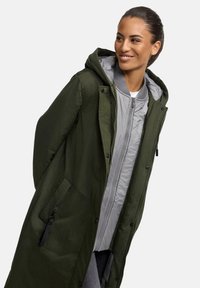 Green parka featuring a gray, quilted lining and hood, with zippered and button closures, and side pockets. Fabric has a smooth texture.