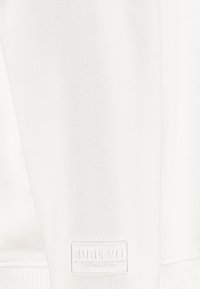 Weißer Kapuzenpullover aus strukturiertem Stoff, mit gerippten Bündchen und einem auffälligen gewebten Etikett mit dem Markennamen "SUBLEVEL."