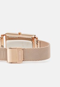 Roségoldenes Mesh-Armbanduhr mit einem rechteckigen Gehäuse aus rostfreiem Stahl, strukturiertem Ziffernblatt und einem polierten Verschluss mit dem Markennamen "SKAGEN."