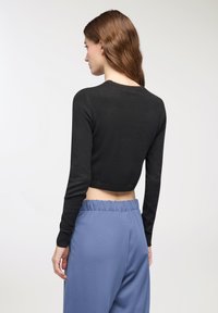 Maglione nero corto con maniche lunghe, realizzato in un tessuto leggero, abbinato a pantaloni blu larghi con cintura elastica.
