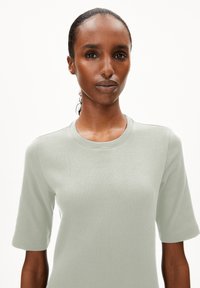 Helles grünes, geripptes Strickoberteil mit kurzen Ärmeln und rundem Halsausschnitt, das über einen strukturierten Stoff und eine figurnahe Silhouette verfügt.