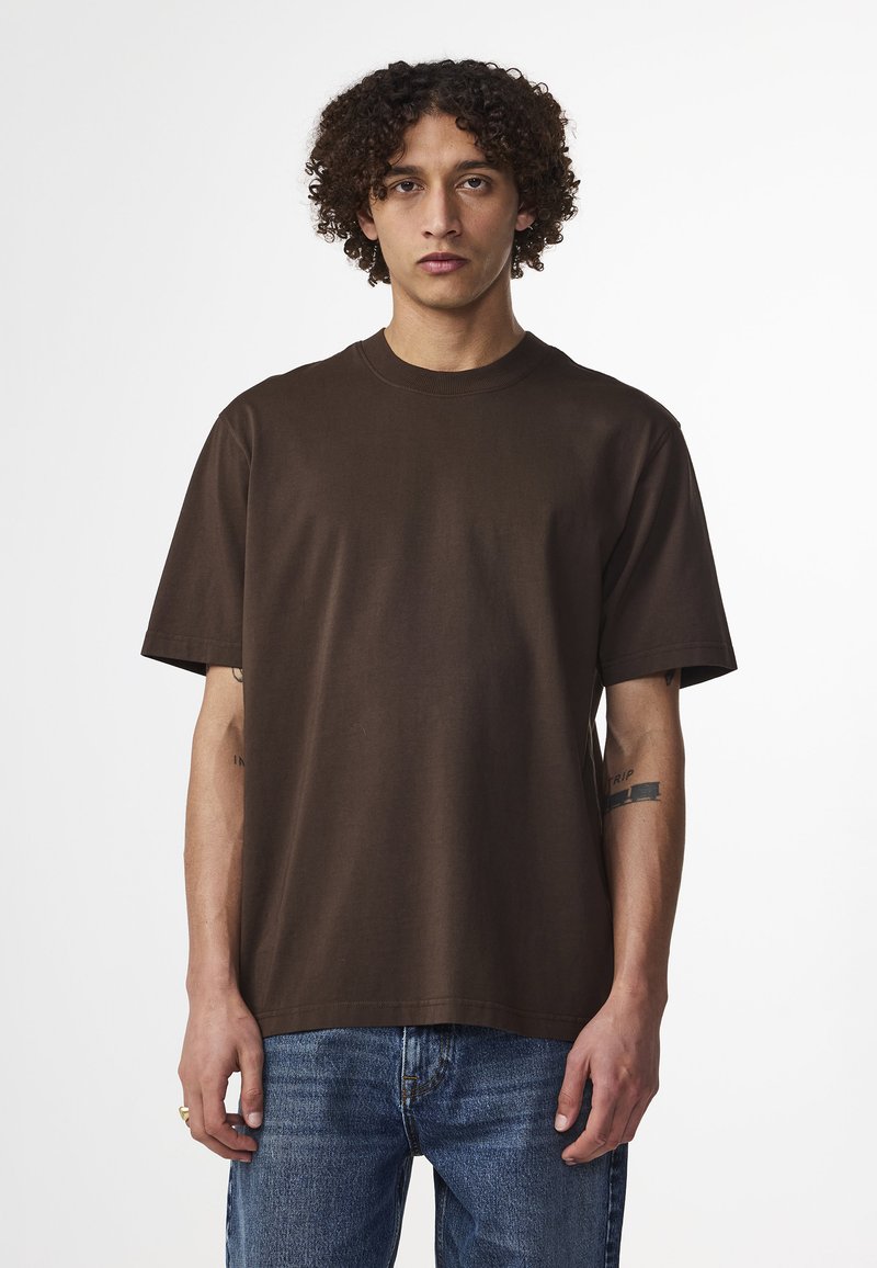 T-shirt girocollo in cotone marrone, maniche corte, vestibilità comoda, texture liscia, con scollo tondo, indossato con jeans in denim blu.