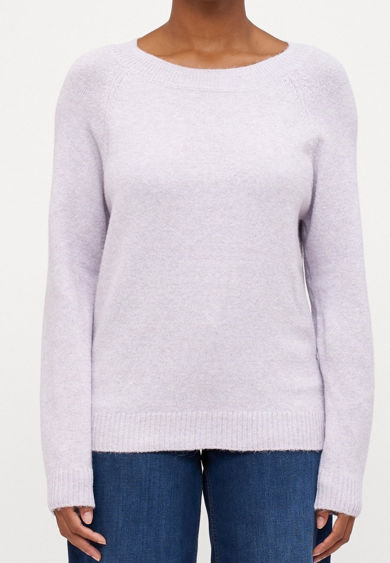 Pull doux lavande à col rond avec manches longues porté avec un jean bleu foncé, montré du cou aux hanches.