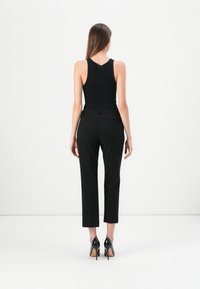 Zwarte aansluitende tanktop met een ronde hals, gecombineerd met zwarte tailor-made broek met riem, zakken en rechte been snit, gestyled met zwarte hakken.