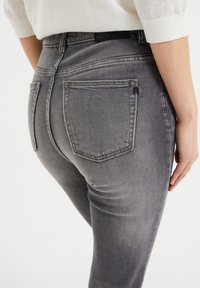 Gray denim jeans with a slim fit, featuring back pockets, a waistband tag, and a slightly faded texture.