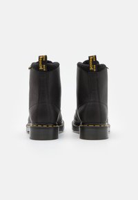 Botines de cuero negro hasta el tobillo con un acabado texturizado, que cuentan con un forro suave, costuras amarillas y tiradores en bucle para facilitar su puesta.