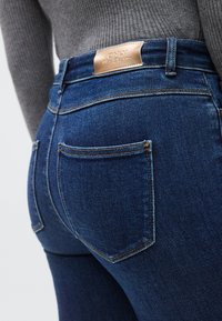 Σκούρα μπλε τζιν με εφαρμοστή γραμμή, διαθέτουν δύο πίσω τσέπες, αντίθετες ραφές και δερμάτινο ταμπελάκι με το λογότυπο στη μέση της ζώνης.