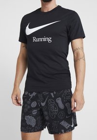 Camiseta de algodón negra con el logo de Nike en blanco y el texto "Running", combinada con pantalones cortos negros que presentan un patrón gráfico y acentos textuales.