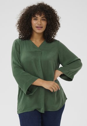 Green, long-sleeve blouse with a V-neck and relaxed fit. Smooth, lightweight fabric with a subtle texture. Notable wide sleeves and curved hem.