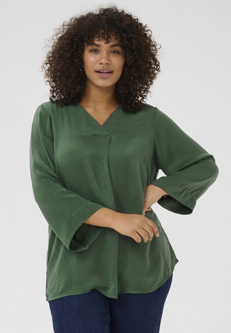 Blusa verde de manga larga con escote en V y corte relajado. Tela suave y ligera con una sutil textura. Manga ancha notable y dobladillo curvado.