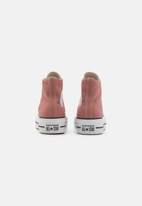 Rosa canvas hög-topp sneakers med vita gummisulor, kontrasterande svarta ränder och en cirkulär logotyp-etikett på sidan.