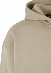 Beige hættetrøje med en blød tekstur, der har en buet halsudskæring og en almindelig pasform. Stoffet virker glat og let.