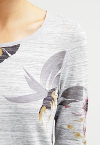 Maglietta grigia chiaro a maniche lunghe con scollatura rotonda, caratterizzata da un design grafico floreale in colori tenui e un tessuto a maglia testurizzato.