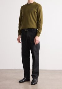 Pull vert olive, jean denim foncé avec couture contrastante, ceinture noire et bottes en cuir noir. Design simple et coupe ajustée.