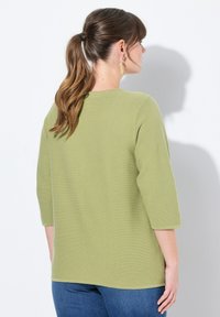 Olivgrön långärmad topp med texturerad yta, rund halsringning och sänkta axlar, kombinerad med blå jeans.