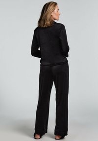 Musta loungewear-setti, joka on valmistettu pehmeästä kankaasta. Setti sisältää rento-mallisen takin, jossa on korkea kaulus, sekä leveälahkeiset housut, joissa on kinkku- ja taitetut hihansuut.