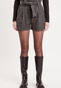 Shorts à carreaux gris avec taille haute et ceinture nouée, associés à des collants noirs transparents et des bottes en cuir noir jusqu'aux genoux.