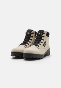 Scarpe da trekking beige con upper in pelle texturizzata, accenti in rete nera, spesse suole in gomma nera e sistema di lacci stratificato. Logo Fila visibile.