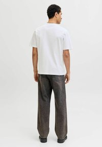 Balta trumpa rankovė t-shirt sukombinuota su tamsiomis, per didelėmis pusiau dėvėtomis džinsinėmis kelnėmis. Paprastas, kasdieniško stiliaus dizainas su neutralių spalvų palete.