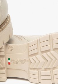 Bottine en cuir beige avec une semelle texturée, présentant un motif de crampons en zigzag, un logo en relief et un détail du drapeau italien au bas.