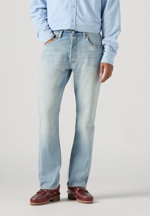 Jeans in denim azzurro chiaro con taglio dritto, dotati di tasche, zip e una leggera sbiaditura. Abbinati a mocassini marroni scuri.