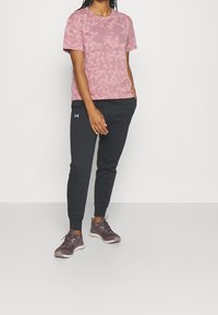 Růžové mramorované tričko se šedým logem v kombinaci s tmavě šedými tepláky. Obuv má šedé a burgundské akcenty. Jednoduchý, neformální outfit.