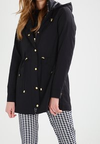 Svart huva jacka med gulddetaljer, elastisk dragsko i midjan och fickdetaljer, matchad med rutiga byxor.