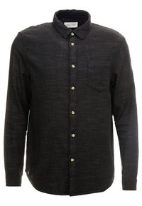 Musta nappipaita, valmistettu teksturoidusta kankaasta. Siinä on kaulus, yksi rintatasku ja etupuolella kullanväriset napit. Pitkät hihat.