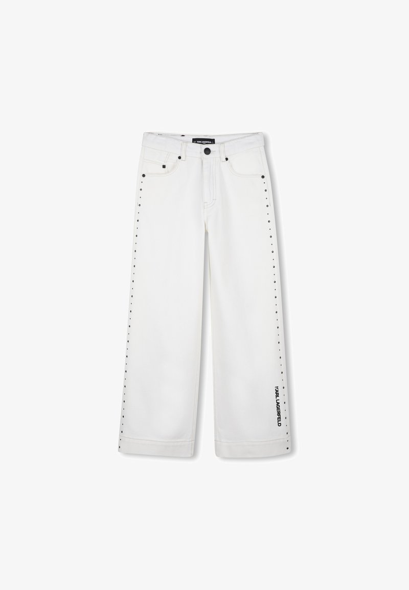Jean blanc à jambes larges en denim, avec des clous noirs le long de la couture latérale et un logo noir sur le bas de la jambe gauche.